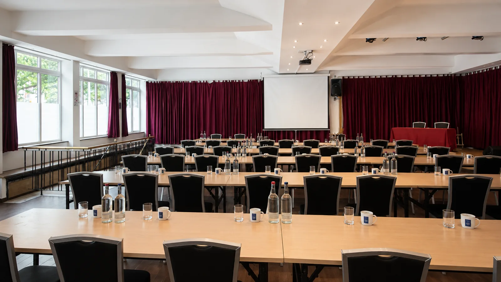 Großer Saal mit Reihenbestuhlung, Leinwand und Bühne