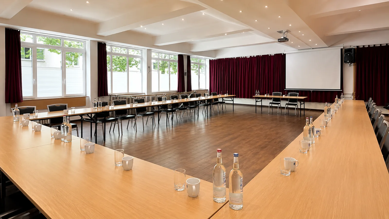 Großer Saal mit großer U-Form-Bestuhlung, Tageslicht und Blick zur Leinwand